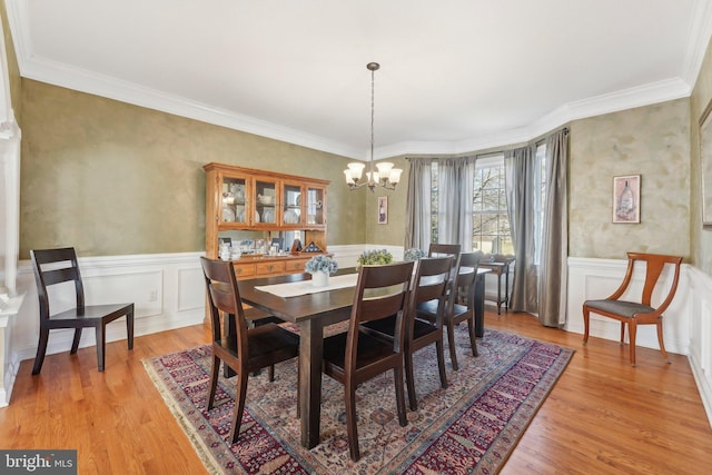 dining area featuring light wood-style flooring, a wainscoted wall, a chandelier, and ornamental molding