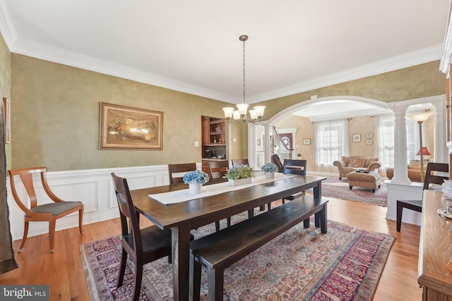 dining room with a wainscoted wall, light wood-style floors, arched walkways, and ornate columns