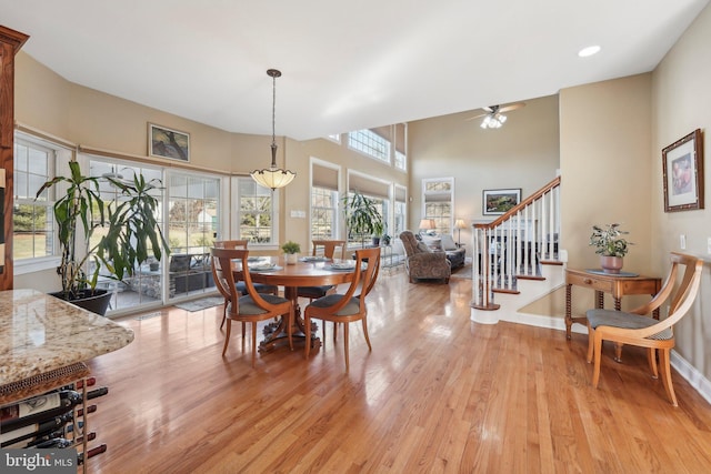 dining area featuring stairway, baseboards, light wood-type flooring, and a high ceiling