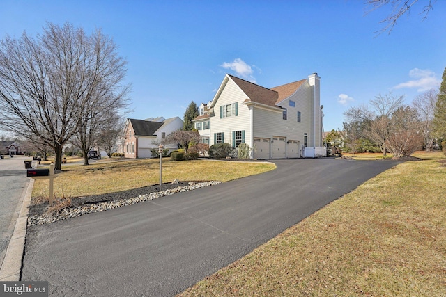 view of side of property featuring aphalt driveway, a yard, a chimney, and a garage