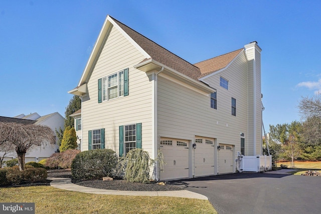 view of side of property featuring driveway, a chimney, a garage, and a shingled roof