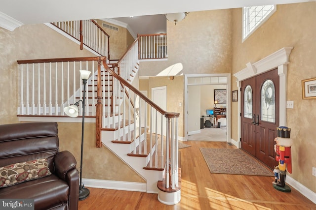 entryway featuring visible vents, wood finished floors, crown molding, baseboards, and stairs