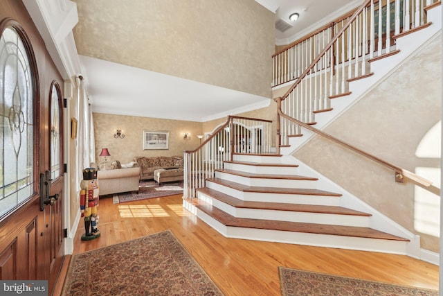 entryway with stairway, wood finished floors, visible vents, a high ceiling, and crown molding