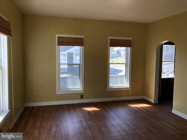 empty room with dark wood finished floors, arched walkways, and baseboards