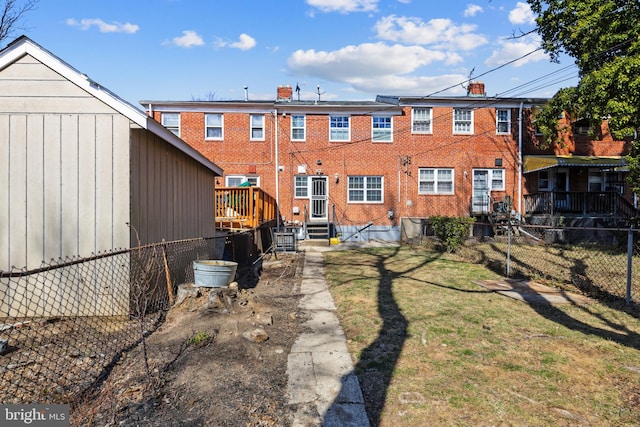 rear view of house with entry steps, fence, brick siding, and a lawn