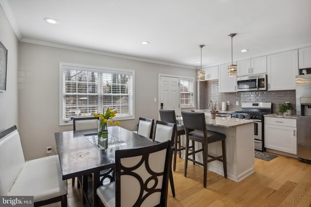 kitchen featuring light wood finished floors, backsplash, stainless steel appliances, and ornamental molding