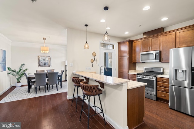 kitchen featuring a kitchen bar, brown cabinets, dark wood-style floors, stainless steel appliances, and a peninsula