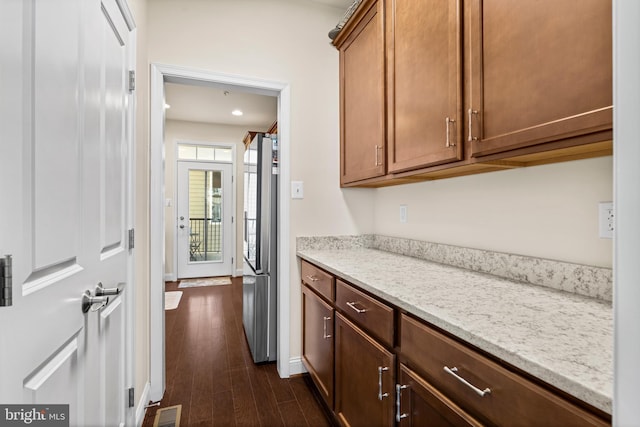 kitchen featuring visible vents, baseboards, dark wood finished floors, light stone counters, and freestanding refrigerator