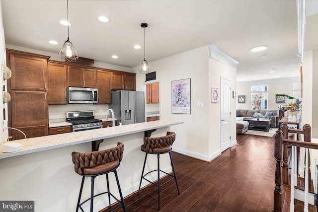 kitchen featuring light stone countertops, dark wood finished floors, pendant lighting, appliances with stainless steel finishes, and a kitchen breakfast bar