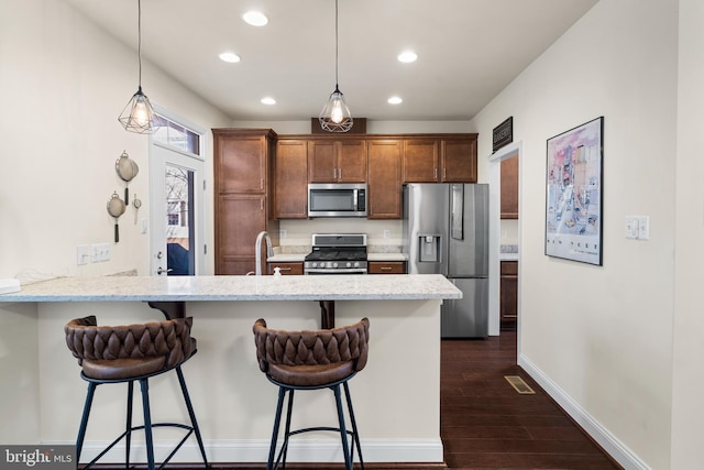 kitchen featuring a peninsula, dark wood-style flooring, a sink, appliances with stainless steel finishes, and a kitchen breakfast bar