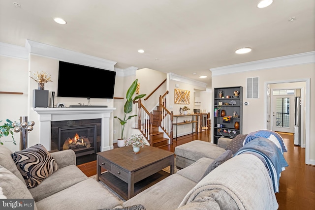 living room featuring visible vents, a fireplace with flush hearth, wood finished floors, stairway, and crown molding