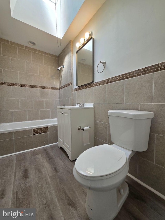 bathroom featuring toilet, vanity, tiled shower / bath combo, wood finished floors, and tile walls