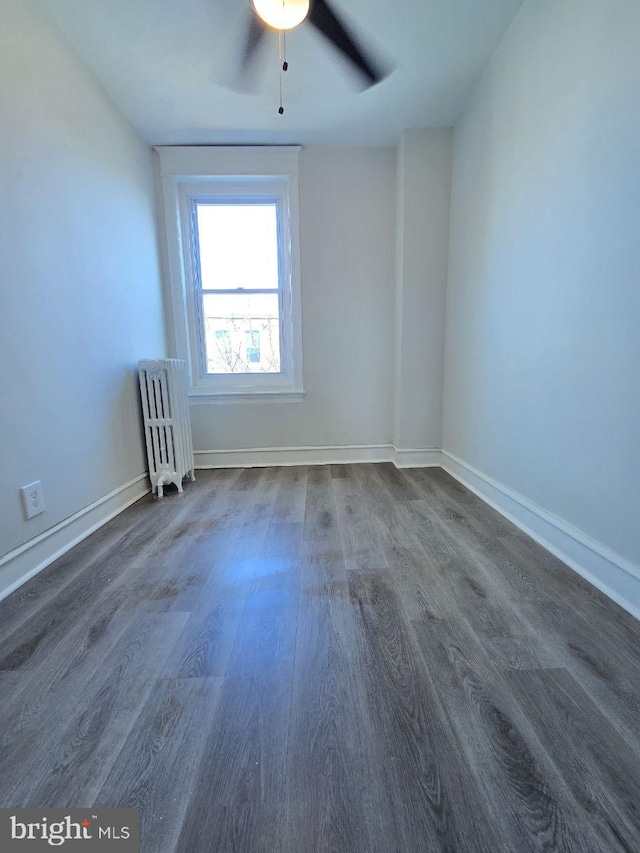 spare room featuring ceiling fan, baseboards, wood finished floors, and radiator heating unit