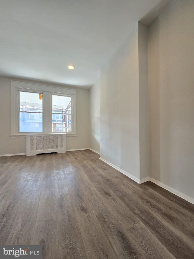 spare room featuring dark wood finished floors, radiator, and baseboards