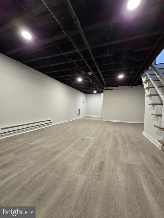 finished below grade area featuring a baseboard radiator, baseboards, wood finished floors, and stairs