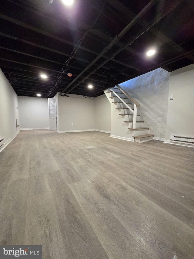 finished below grade area with stairs, wood finished floors, baseboards, and baseboard heating