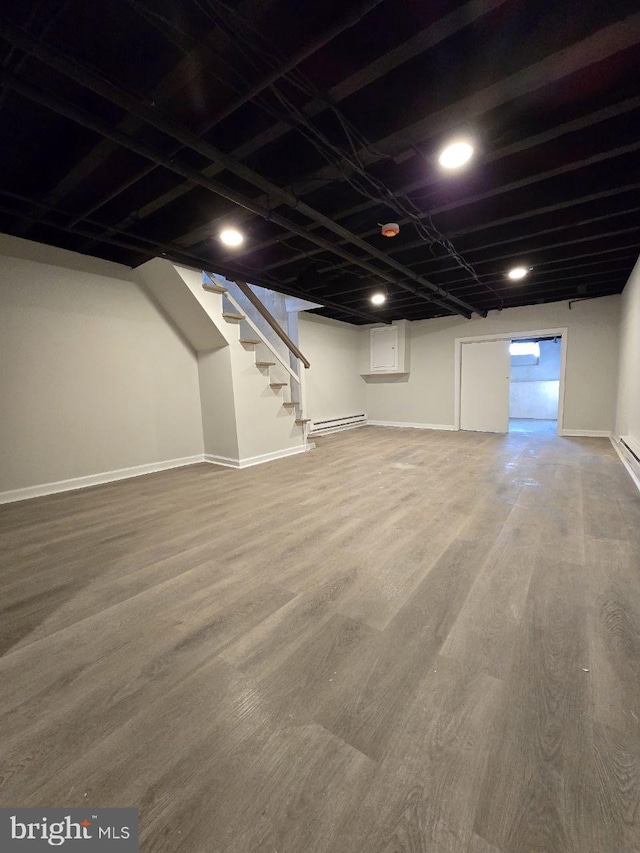 finished basement featuring a baseboard heating unit, baseboards, wood finished floors, and stairs