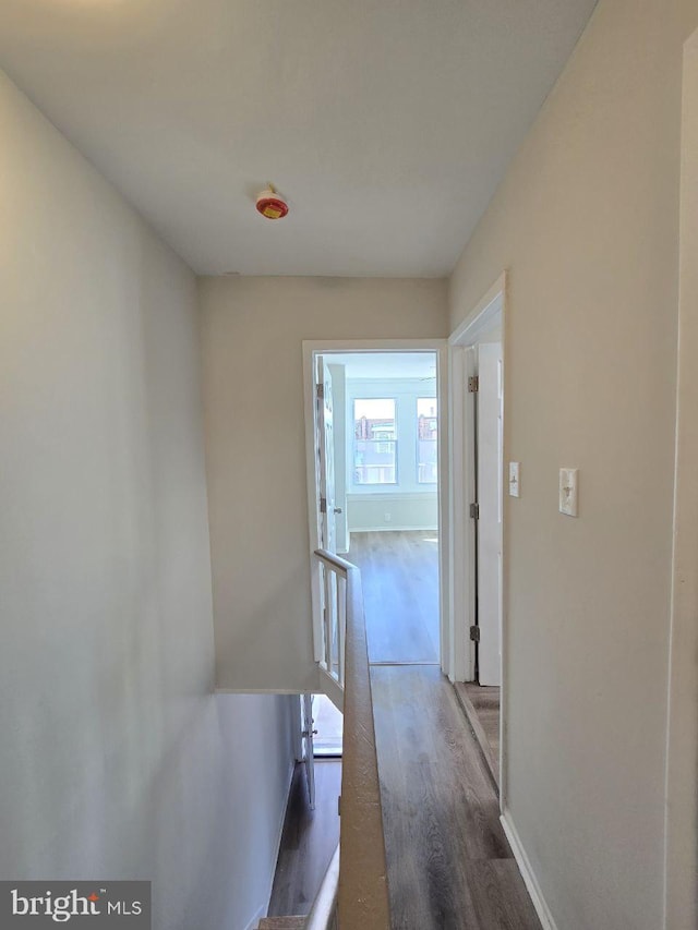 hallway featuring wood finished floors, an upstairs landing, and baseboards