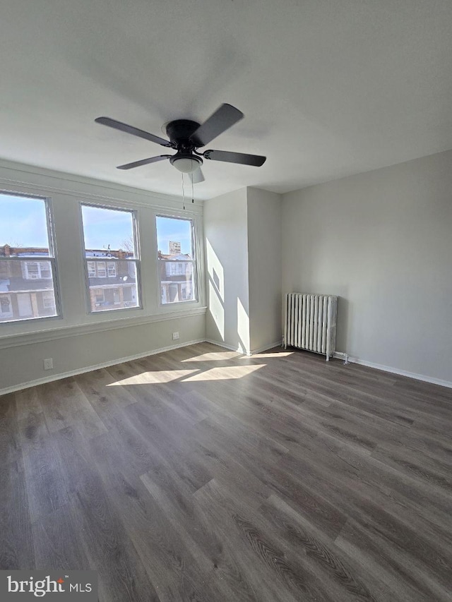 spare room with radiator heating unit, dark wood-style floors, baseboards, and ceiling fan