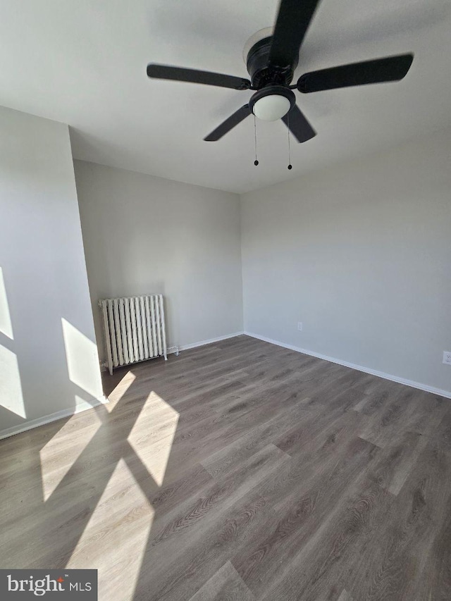 spare room with ceiling fan, baseboards, wood finished floors, and radiator heating unit