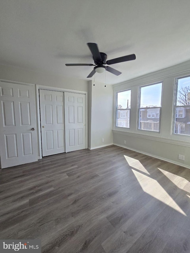 unfurnished bedroom featuring a closet, dark wood finished floors, a ceiling fan, and baseboards