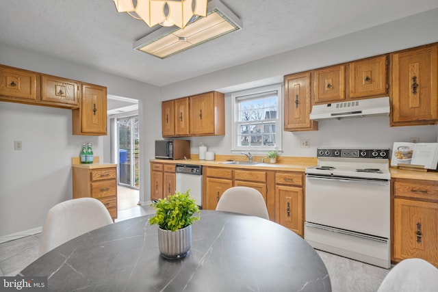 kitchen featuring white appliances, brown cabinets, under cabinet range hood, and a sink