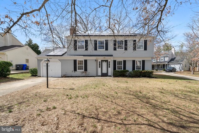 colonial home with solar panels, a front lawn, concrete driveway, a chimney, and a garage