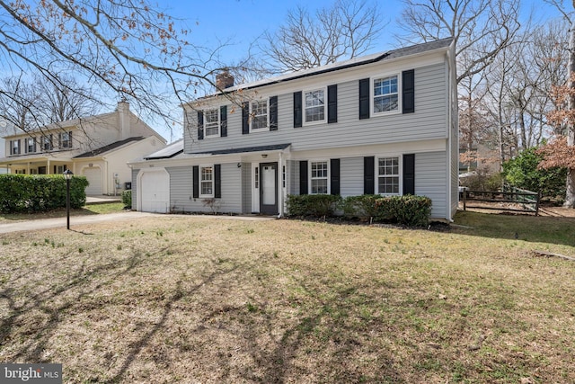 colonial home with a front yard, driveway, solar panels, an attached garage, and a chimney