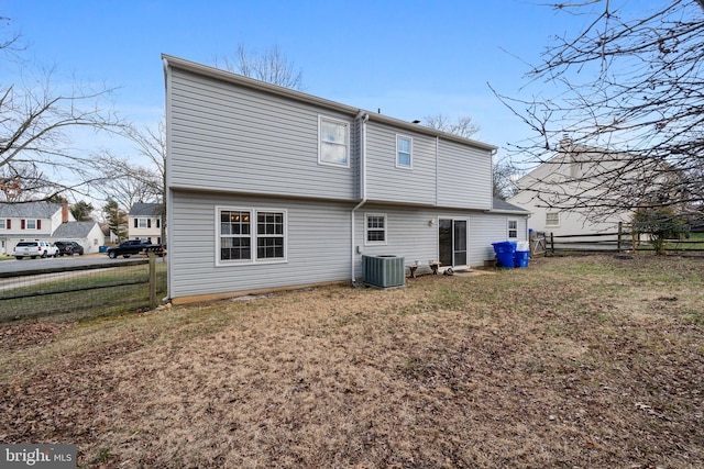 rear view of house with cooling unit, a lawn, and fence