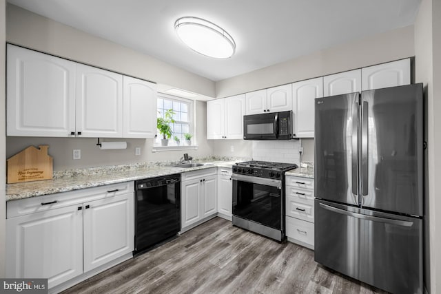 kitchen featuring light stone counters, light wood finished floors, a sink, black appliances, and white cabinets