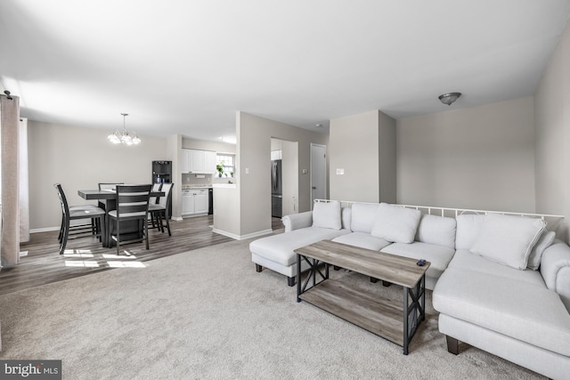 carpeted living area with wood finished floors, baseboards, and a chandelier