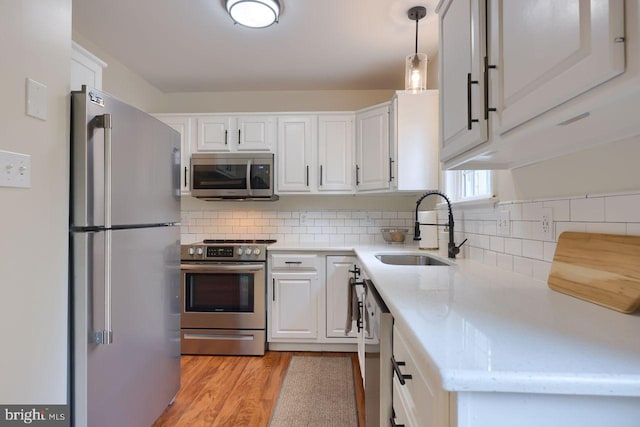 kitchen with light wood-style flooring, a sink, appliances with stainless steel finishes, white cabinetry, and backsplash