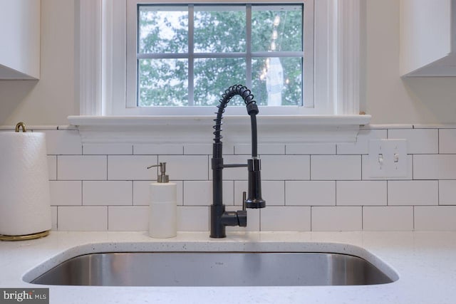 interior details with a sink, decorative backsplash, light stone countertops, and white cabinetry