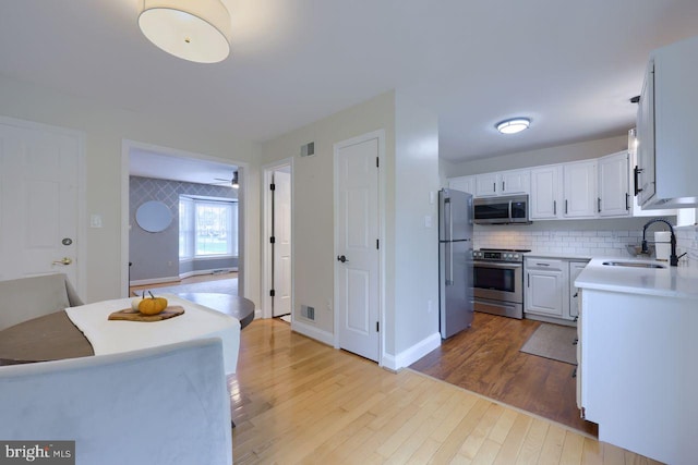 kitchen with tasteful backsplash, visible vents, wood finished floors, stainless steel appliances, and a sink