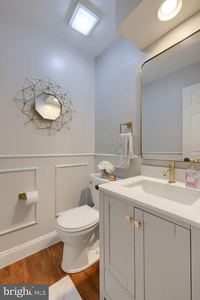 half bath with vanity, toilet, and wood finished floors