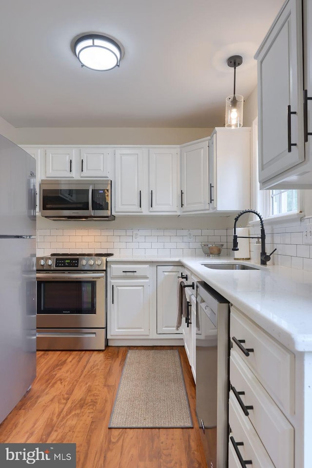 kitchen featuring a sink, decorative backsplash, stainless steel appliances, white cabinetry, and light wood-type flooring