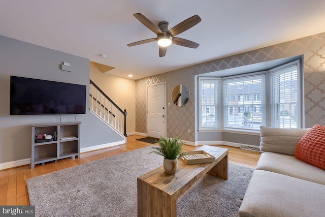 living area featuring stairs, wood finished floors, baseboards, and wallpapered walls