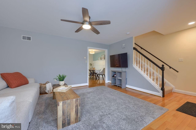 living area with visible vents, baseboards, stairway, wood finished floors, and a ceiling fan