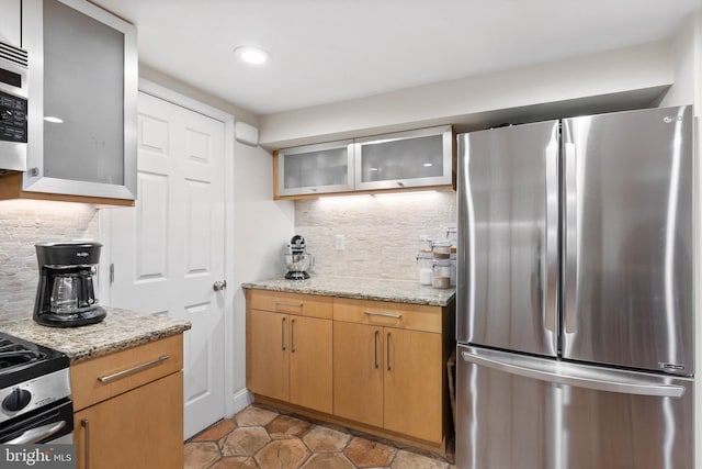 kitchen featuring decorative backsplash, light stone countertops, glass insert cabinets, and appliances with stainless steel finishes