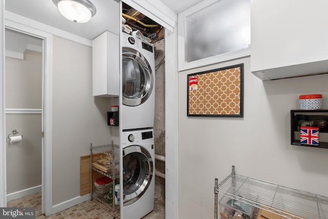 washroom with cabinet space, baseboards, and stacked washing maching and dryer