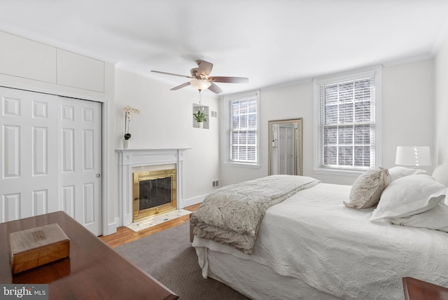 bedroom with visible vents, a fireplace with flush hearth, a ceiling fan, wood finished floors, and a closet