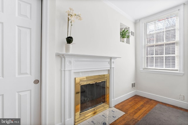 details featuring visible vents, baseboards, a tiled fireplace, ornamental molding, and wood finished floors