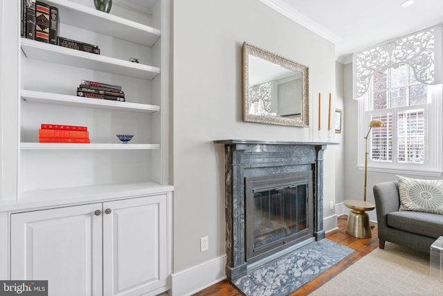 living area featuring a fireplace with flush hearth, wood finished floors, baseboards, and ornamental molding