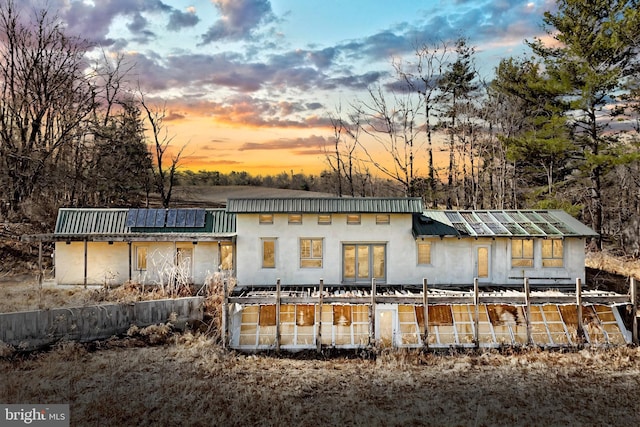 back of property at dusk with solar panels, metal roof, and stucco siding