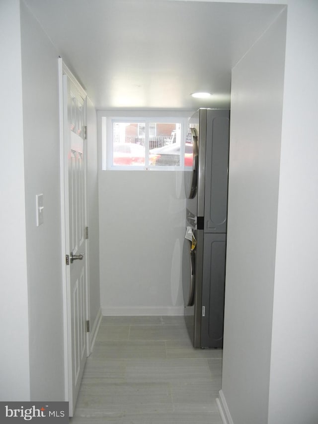 hallway featuring stacked washer / drying machine and baseboards