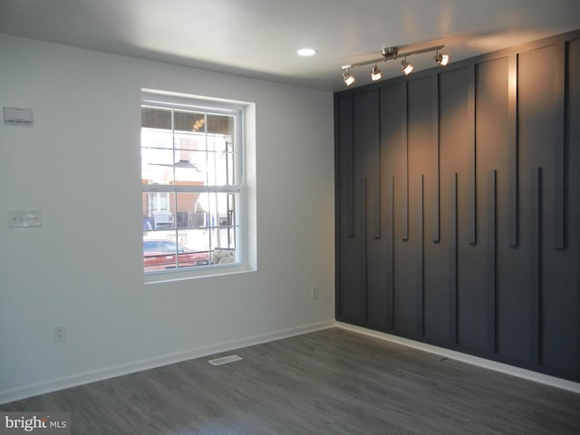 empty room featuring visible vents, track lighting, baseboards, and dark wood-style flooring