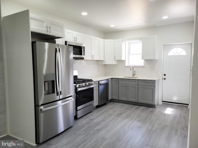 kitchen with a sink, stainless steel appliances, light wood-style floors, light countertops, and decorative backsplash