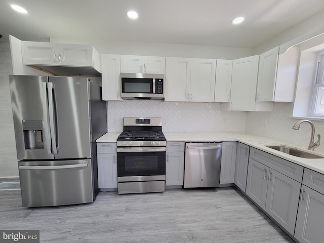 kitchen featuring light wood finished floors, gray cabinetry, light stone counters, stainless steel appliances, and a sink