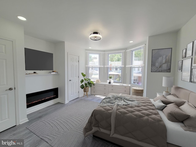 bedroom featuring recessed lighting, baseboards, wood finished floors, and a glass covered fireplace