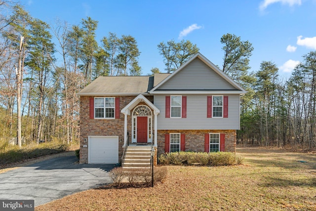 bi-level home featuring aphalt driveway, an attached garage, stone siding, and a front yard